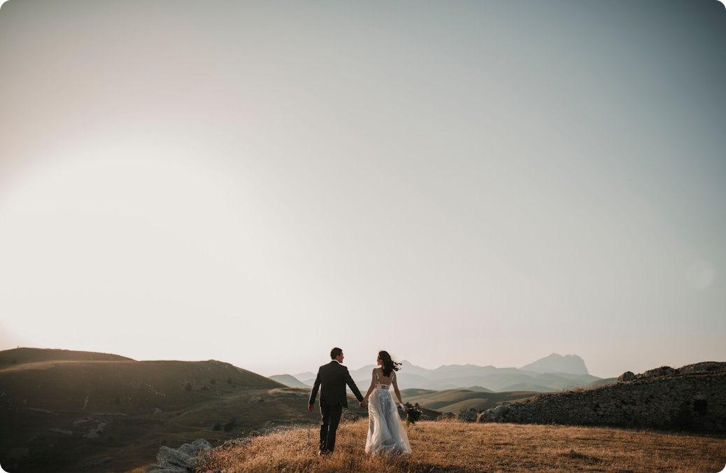 Photo montrant un couple en haut d'une colline en vêtements de mariés et se tenant par la main